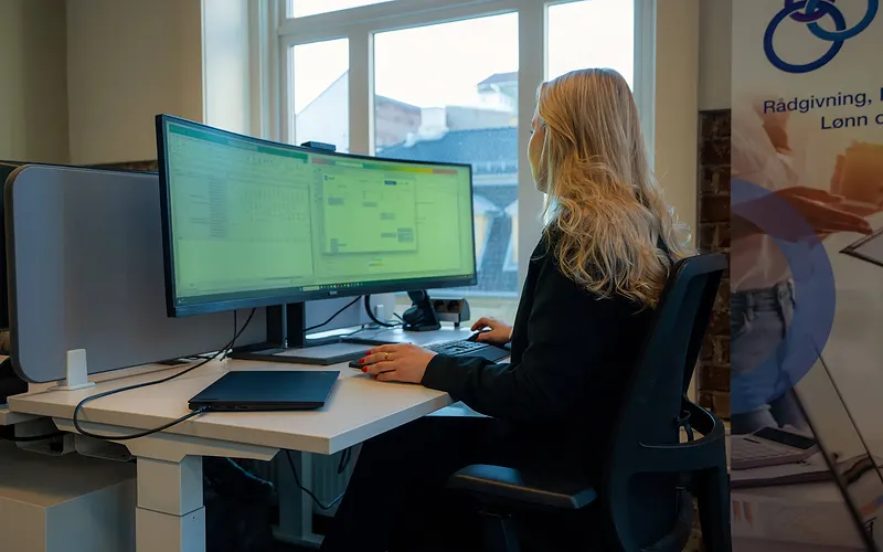 Kollega med långt ljust hår arbetar vid en bred, böjd skärm, sedd från sidan