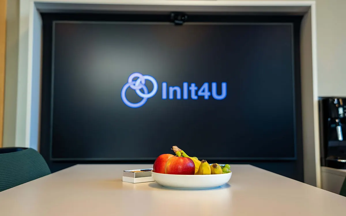 Mötesrum med InIt4U-logotypen på en stor skärm och en fruktskål på bordet
